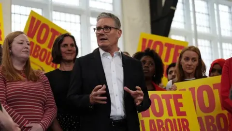 PA Media Keir Starmer in dark suit and white shirt addressing a group of activists holding yellow placards with red writing which reads Vote Labour