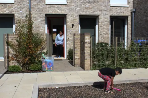 BBC A mother watches as her son plays in the front garden