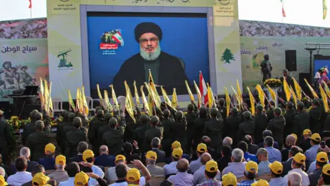 AFP Hezbollah members salute as the Lebanese group's leader, Hassan Nasrallah, addresses a rally in al-Ain (25 August 2019)