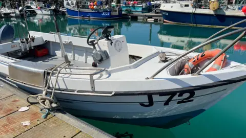 A small fishing vessel is moored at harbour in warm sunny waters.