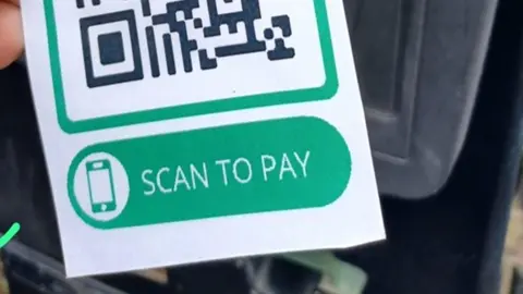 A QR code sticker with the words "scan to pay" that was stuck on a parking ticket machine in Stroud as part of a scam