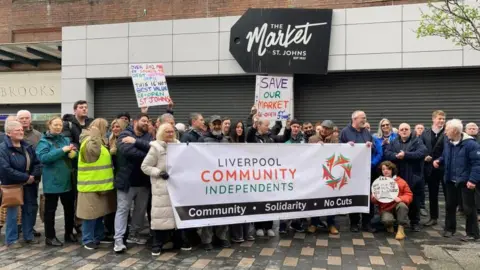 A group of traders hold a number of signs outside the market as they protest against its closure