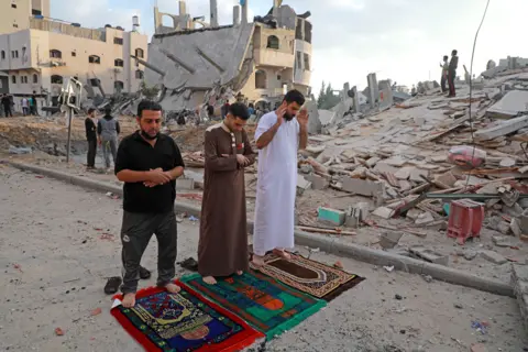 Majdi Fathi / Getty Images Muslim men perform the morning Eid al-Fitr prayer with destroyed buildings behind them in Beit Lahia in the northern Gaza Strip