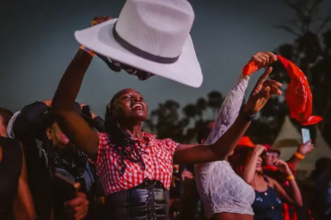 FREDRIK LERNERYD / AFP / GETTY IMAGES  Revellers line dance during the International Cowboy Day at Ngong race course. They wave cowboy hats and bandannas in the air.