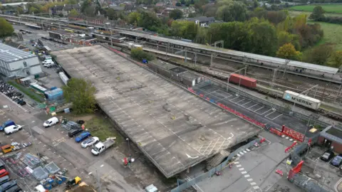 Aerial photo showing the empty top deck of a car park next to the railway line at Colchester station, Other cars are parked nearby along with a builder's skip and temporary buildings,