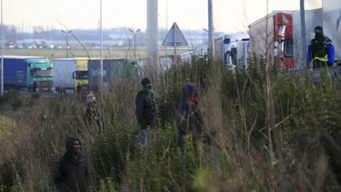 Reuters Migrants on a roadside embankment beside a line of lorries near Calais