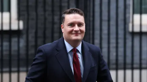 Reuters Wes Streeting is pictured walking away from 10 Downing Street in London. He is wearing a dark blue jacket, light blue shirt and red tie. He has short brown hair and is clean shaven. 