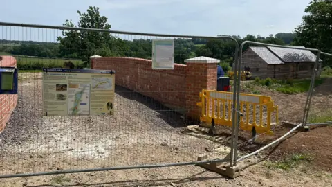 A partly-built bridge at Pewsham locks over the canal with scaffolding around it and lots of green space and trees in the background.