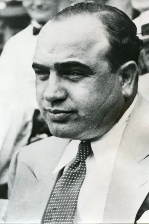 Getty Images A balding Al Capone wearing a light coloured suit. He is smiling into the distance and his trademark scar is visible on his left cheek 