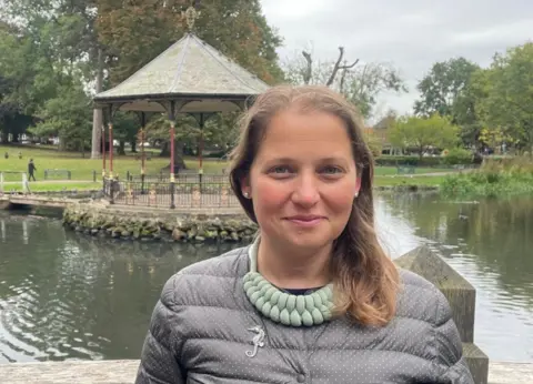 Local Democracy Reporting Service A woman with brown hair and a grey top is looking at the camera. A bandstand, which is next to water, is behind her on the photo. 