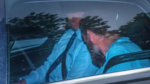 PA Media Simon O’Donovan (right) arrives to appear before a sitting of the Special Criminal Court in Dublin. He is inside a car with his face turned away. An officer is sitting beside him with their face pixalated.