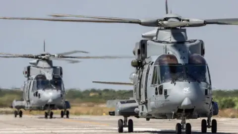 UK MOD  Two Merlin Mk4 helicopters on a runway. One is in front of the other