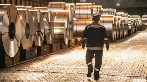 A worker walks past coils of finished steel at the Thyssenkrupp steel mill in Duisburg, Germany. Photo: 20 March 2025