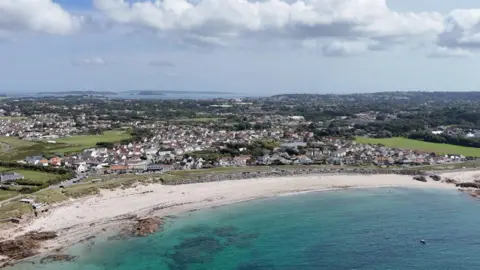 A view of a Guernsey bay form above. It shows a sweeping beach with blue water and housing.