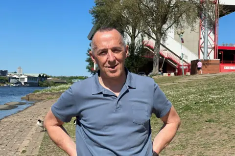 Andy Caddell standing in front of the City Ground, with part of the River Trent visible