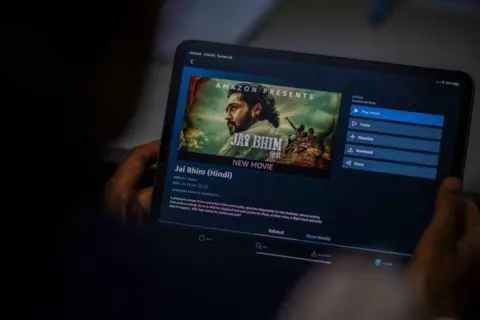 Getty Images In this photo illustration taken on November 30, 2021, a man prepares to watch the Hindi dubbed Tamil legal drama 'Jai Bhim' on the Amazon Prime Video app in New Delhi. -