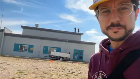 Community TV / ComTV.ca Thomas Fougere of Community TV reporting from outside the school while two followers of Ms Didulo, standing on the roof, look on