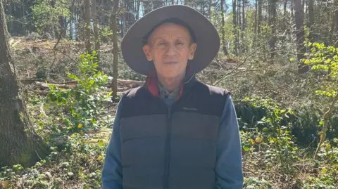 A man wearing a hat and a gilet standing in a forest