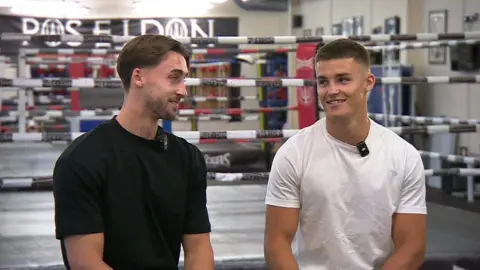 Owen (left) and Taylor Bevan pose for a photo with a boxing ring behind them