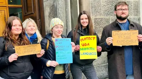 Students holding protest signs about protecting modern languages.