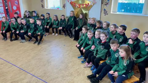 A group of children in school uniforms sit on the floor