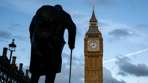 Getty Images A Sir Winston Churchill statue seen in front of Big Ben in central London. The stature is in silhouette along with some buildings to the left, and Big Ben is in full colour. The picture was likely taken at dusk as the sky is beginning to go dark.