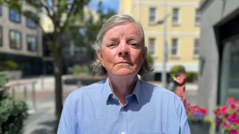 BBC A man with medium length grey hair, wearing a blue shirt looking towards the camera.
