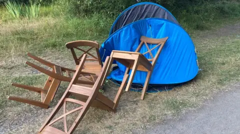 Hazlerigg Parish Council An abandoned set of dining chairs and a blue tent which has been dumped by the side of a path.