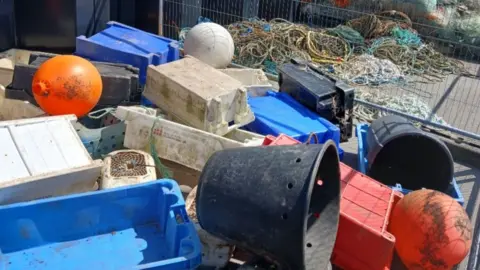 East Suffolk Council Plastic buckets and trays have been piled up on the side of a dock. The plastic items are black, blue, white, red and orange.