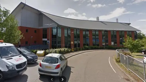 Loddon Valley Police Station - a red brick building that curves with the curve in the road. It has lots of windows. There are two cars and a van parked up to the right in the foreground.