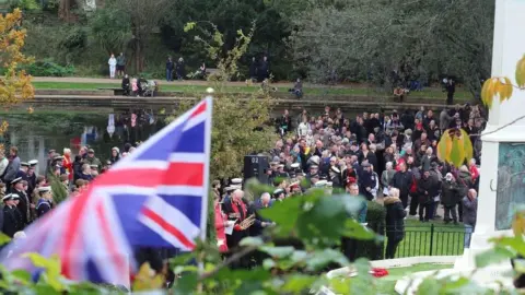 A memorial service held at Alexandra Park in Hastings. Servicemen and members of the public stand in front of a war memorial.