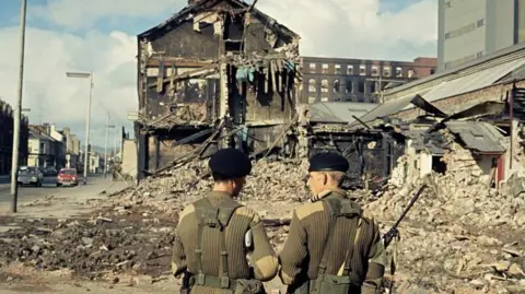 BBC Two British soldiers stand in front of the rubble of destroyed buildings in 1970s Belfast