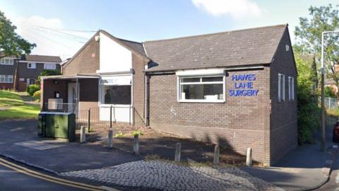 A small brick-built surgery on a residential estate with blue perspex lettering reading "Hawes Lane Surgery"