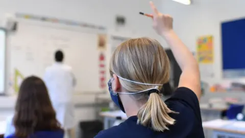 Getty Images A pupil wearing a mask raises her hand in a classroom