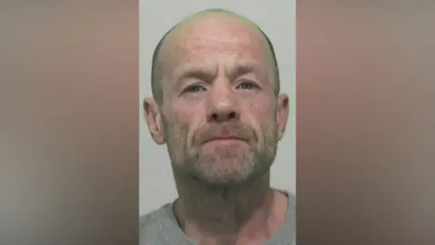 Mugshot of Thomas Brand. He has grey stubble and is bald.