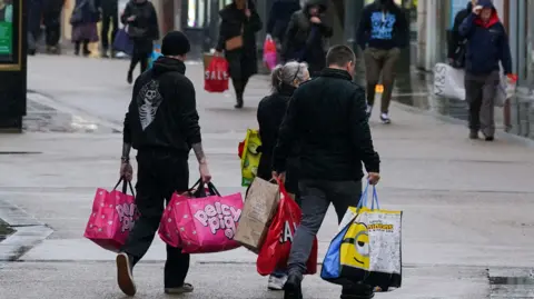 Jacob King/PA Wire Three shoppers clutching Percy Pig shopping bags, walking down Worcester High Street.
