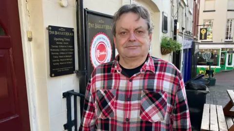 Duncan Borrowman, del pub Bailey Head en Oswestry, estaba afuera del pub en la calle principal. mirando a la cámara vestía una camisa de cuadros negros y rojos.