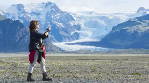 A photographer takes a picture of a landscape in Iceland