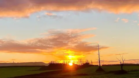 SantaSusie Sunrise with orange sky/clouds and green fields in the foreground at Berkeley in Gloucestershire