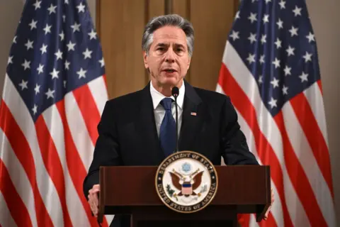 Getty Images Antony Blinken stands at a podium in front of American flags