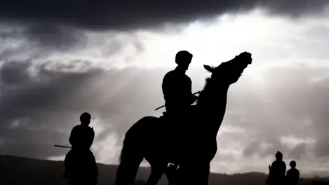 PA Media A horse and rider are silhouetted against a bright sky early in the morning on day two of the Cheltenham Festival 2026