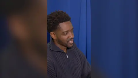 A man with short black hair wearing a blue jumper