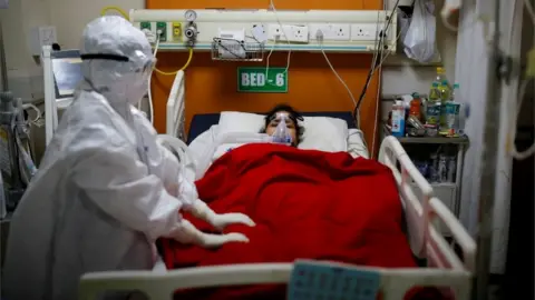 Reuters Woman in hospital bed with doctor in PPE