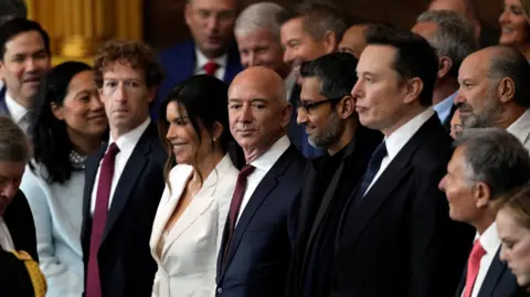 Appearing at the second inauguration of Donald Trump, from left to right: Mark Zuckerberg in a black suit, white dress shirt and red necktie; Jeff Bezos in a navy suit, white dress shirt and red neck tie; Sundar Pichai in an all black suit, shirt and neck tie; Elon Musk in a black suit, white dress shirt and navy neck tie