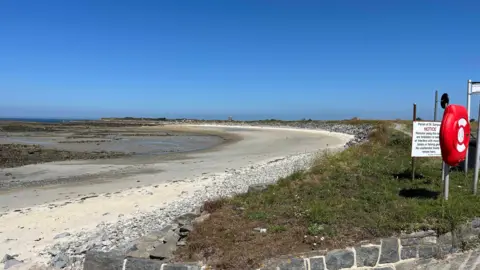 A long sandy beach with a lifebelt holder and a sign.