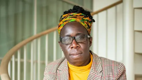 PA Media Still of Ms Adoo-Kissi-Debrah in an orange and green headscarf, yellow jumper and tweed jacket