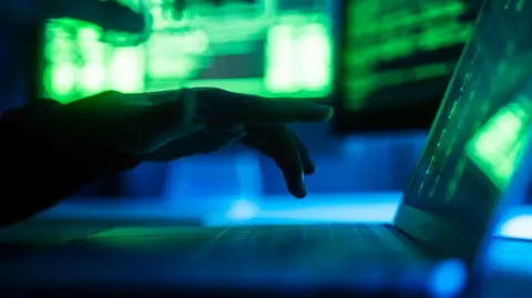 Getty Images A hand in the shadows hovers above a laptop. 