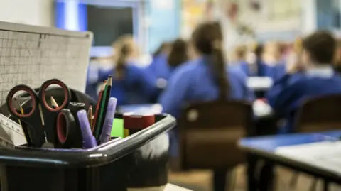 Blurred out children in blue school uniforms sit in a classroom.