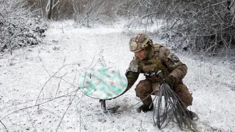 Reuters A soldier sets a Starlink dish down in a snowy field