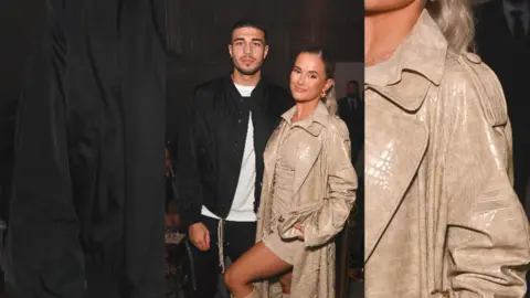 Tommy Fury and Molly-Mae Hague stand next to each other. Tommy wears a white t-shirt and a black jacket. Molly-Mae wears a beige dress and jacket.